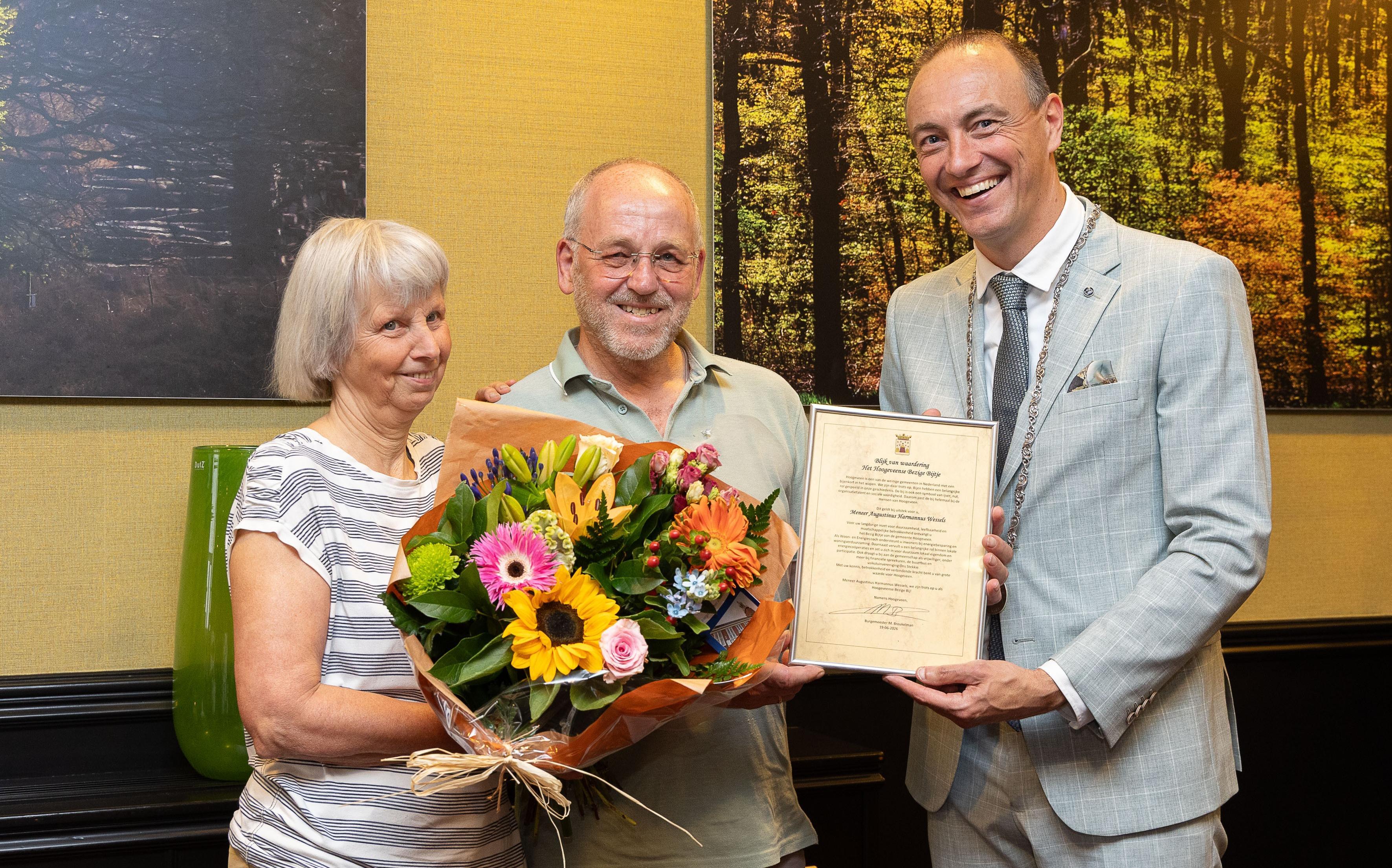 Loco burgemeester Jeroen Westendorp overhandigt Guus Wessels de oorkonde horende bij het Bezig Bijtje Voor zijn echtgenote Yvonne waren er bloemen Foto André Weima