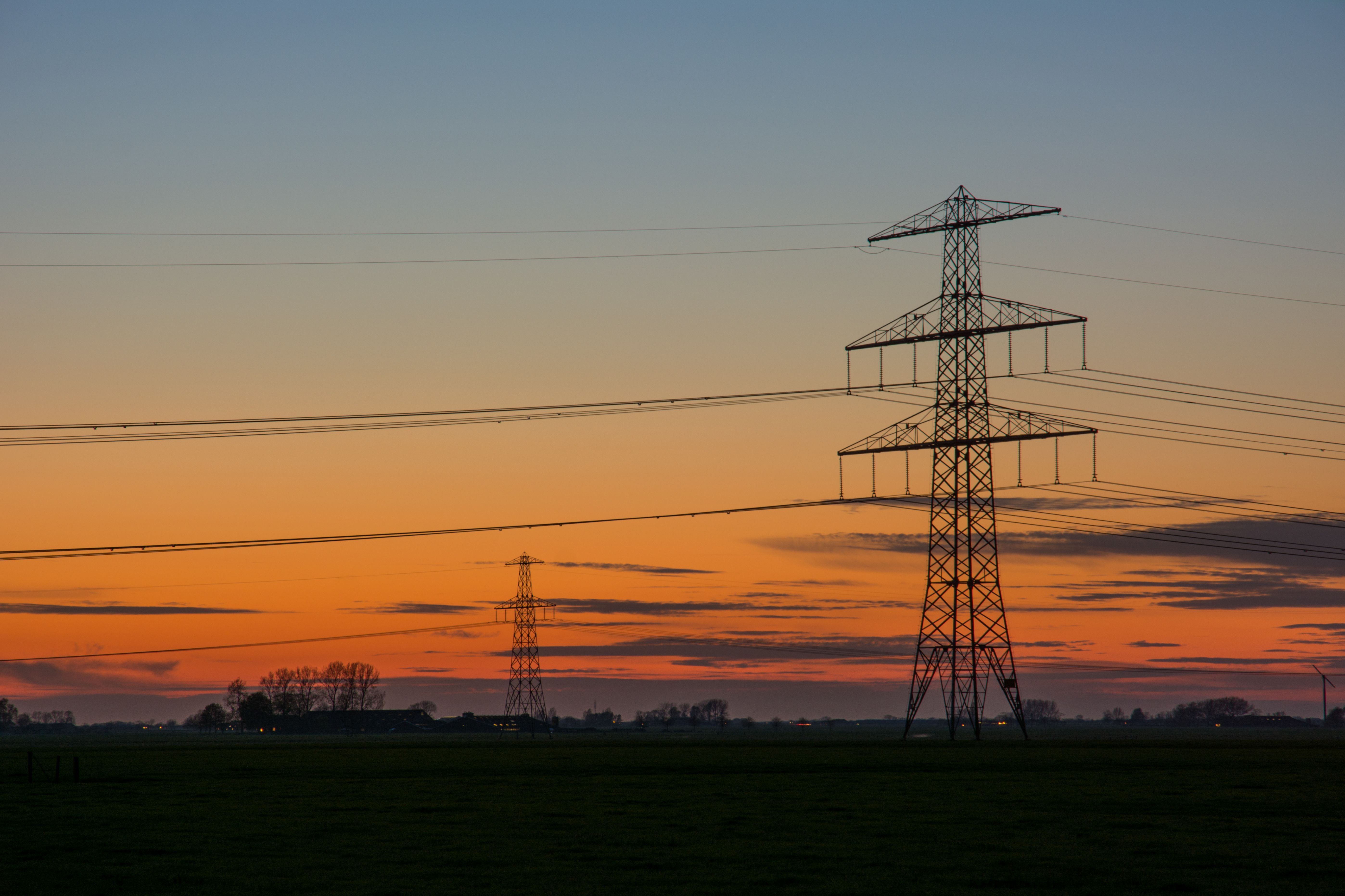 Silhouet van hoogspanningslijnen tegen een levendige zonsonderganglucht op het platteland